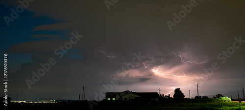 Powerful lightning discharges during a thunderstorm at night over rural farmhouse silhouette and power lines
