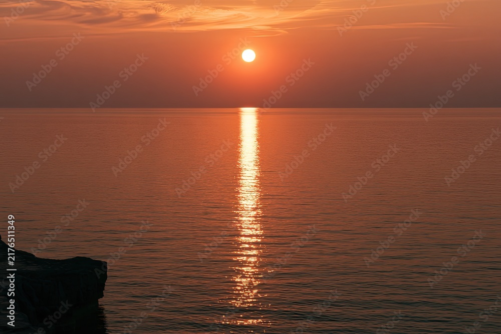 Obraz premium Fiery sun descends over calm ocean, casting golden reflection
