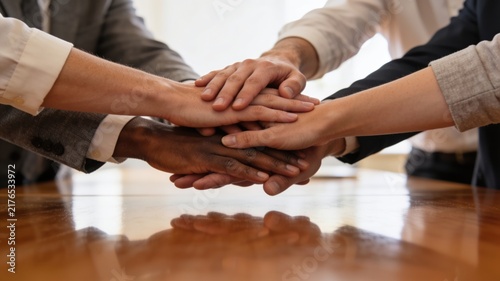 Diverse Business Team Stacking Hands on Wooden Table, Symbolizing Teamwork and Unity
