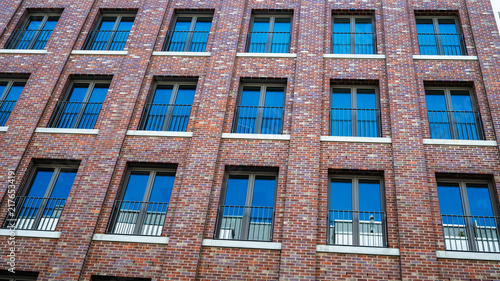 Fotografía Modern red brick building facade with rows of windows reflecting blue sky