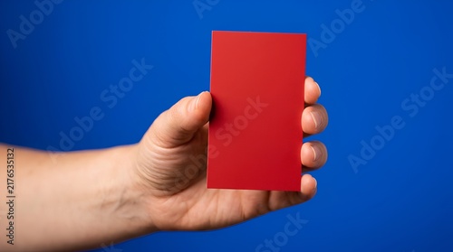 Hand holding blank red color sample card against vivid blue studio background, minimalist design template, high contrast palette swatch mockup for branding, graphic design, paint chip reference and