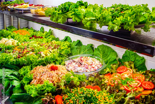 Bild auf Leinwand Vibrant self-service salad bar featuring a rich variety of fresh greens, sliced tomatoes, mixed vegetables, and fruit salads on a buffet counter