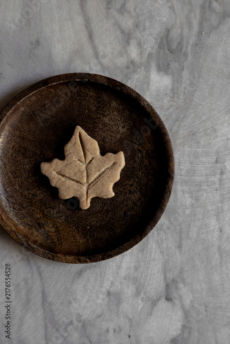 Maple leaf biscuit served in a wooden plate positioned on light grey marble. 