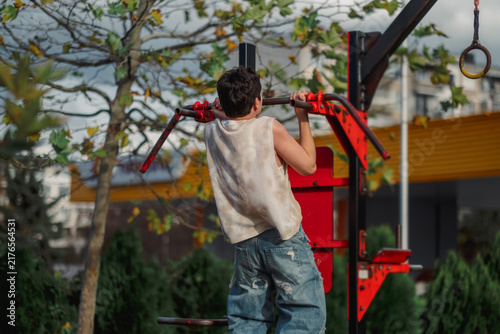 Fotografie Teenage boy lifting himself on a bar seen from behind