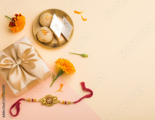 Rakhi Celebration Gift With Sweets, Marigold Flowers and Traditional Raksha Bandhan Bracelet on Pastel Background