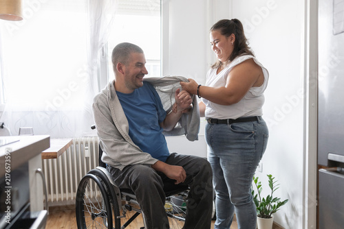 Картината върху платно Personal assistant helping a wheelchair user put on a hoodie during his daily dressing routine at home, inclusive living theme