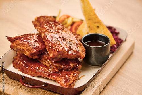 Grilled barbecue ribs served with sauce and side dishes on wooden platter