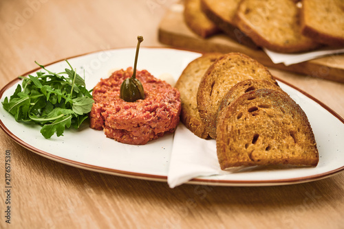 Beef tartare served with toasted bread and arugula on a white plate