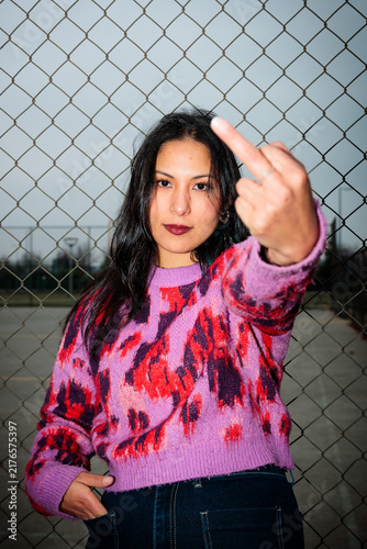 Edgy young latina woman showing middle finger gesture outdoors with direct flash