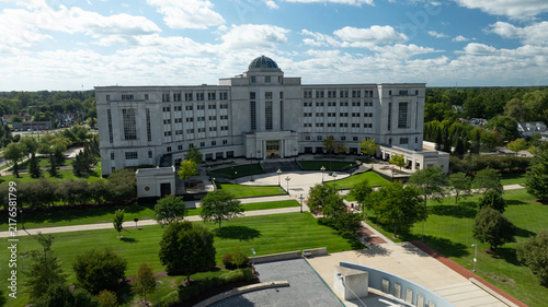 Aerial view of the Michigan Supreme Court building surrounded by lush green trees, manicured lawns, and American and state flags flying in Lansing, Michigan, United States.