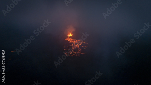 Aerial view of a glowing volcanic eruption at night with molten lava flowing through dark smoke and volcanic ash in Reykjavik, Reykjavikurborg, Iceland.