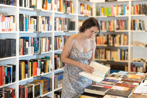 Konstfotografi Adult female reader explores aisles of bookstore, looking for new title to enjoy