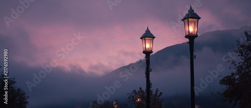 Two illuminated street lamps stand against a dusky mountain backdrop.