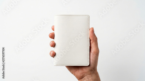 Hand holding a white passport cover with a subtle textured design