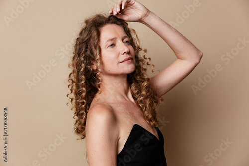 Authentic beauty of a middle aged woman with natural skin without retouching. Portrait of mature female with curly hair posing gracefully in studio. Concept for body positivity.