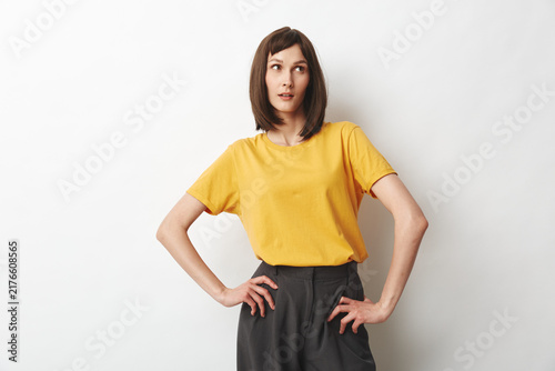 Foto A confident woman in a yellow top strikes a bold pose against a plain backdrop, hands on hips, showcasing casual professional style and self-assured attitude