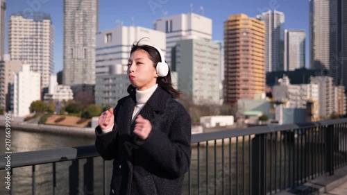 ヘッドフォンで音楽を聴きながら歩道を歩く女性のフォローショット