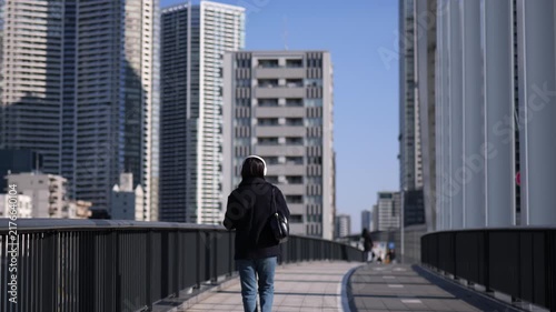ヘッドフォンで音楽を聴きながら歩道を歩く女性の後ろ姿