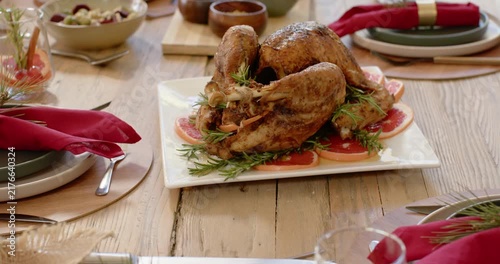 Camera is pulling back to show roasted turkey on platter on rustic dining table during Christmas