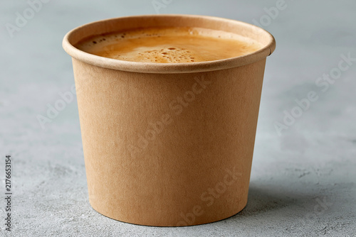 Kraft paper cup filled with freshly brewed espresso coffee on a gray surface