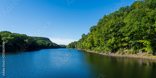 Peaceful scenic view of a forest-covered lake surrounded by trees and rolling hills beneath a clear blue summer sky in Connecticut.