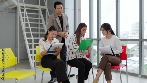 A professional male mentor training his young Asian business team in a modern office, discussing project details with papers during a corporate workshop seminar.