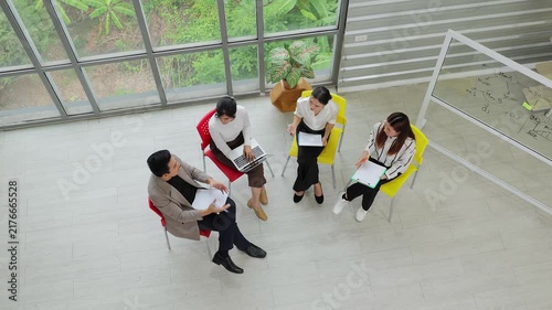 High angle view of young Asian entrepreneurs holding a business meeting in a modern creative office. Diverse team brainstorming and sharing ideas together for startup success.