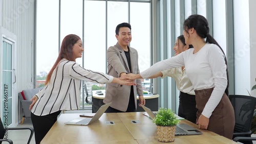 Group of happy Asian business people stack hands together in office meeting room. Diverse coworkers celebrating project success and unity, showing professional teamwork cooperation.