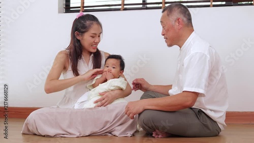 Warm portrait of an Asian grandfather, daughter, and infant grandson. They are sitting together indoors, expressing happiness, love, and strong family relationships across generations.