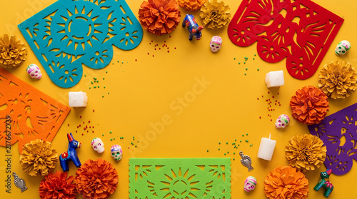 Day of the Dead flat lay with felt papel picado marigolds and sugar skulls on yellow background