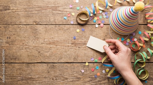 Hand holding blank tag with party hat and confetti on rustic wooden table