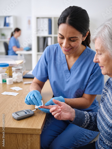 Caring nurse performing a blood glucose test on an elderly patient in a clinic