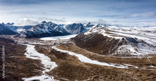 Фотография A vast high-altitude landscape with snow-capped mountains, frozen rivers and barren valley under a clear sky
