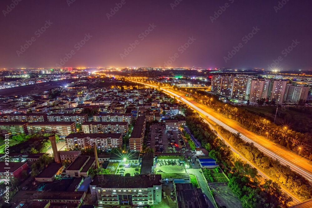 Fototapeta premium High-angle shot of a night cityscape featuring residential buildings and a busy expressway with light trails.