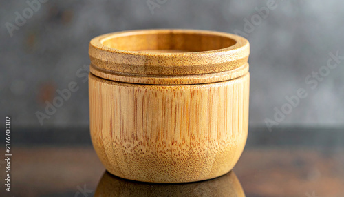 Bamboo Container Close-up: A simple yet elegant bamboo container, showcasing its natural wood grain and circular design, rests on a polished surface against a textured backdrop.