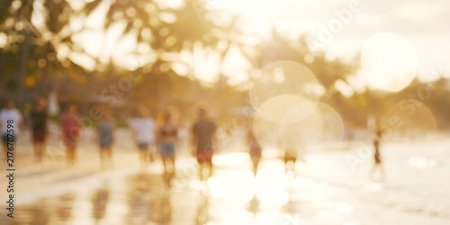 A blurred sunset beach scene with people walking along the shore, palm trees framing the background. Soft golden light creates a warm atmosphere.