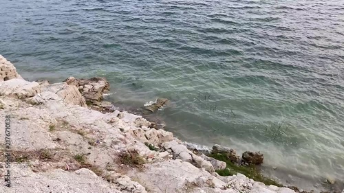 Tropical ocean water waves crash against a rocky cliff. Illustration of a sea, lake, and river scene at sunset and on a windy day. Natural raw video footage, no video edit and real time outdoor shoot