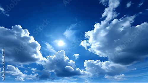 Bright sun shining through fluffy white cumulus clouds in a deep blue sky.
