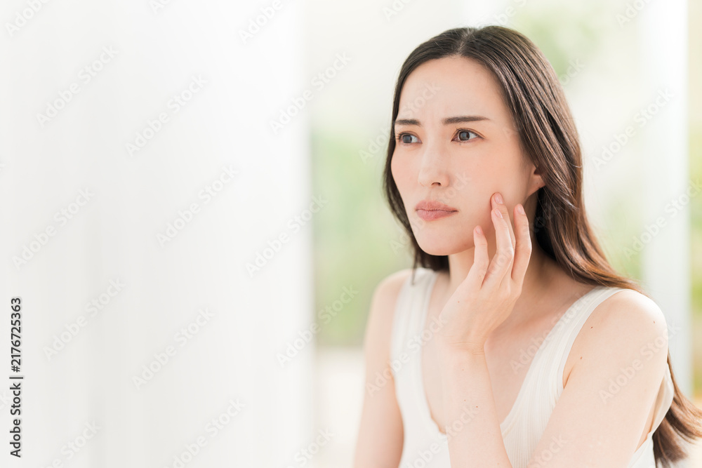 Naklejka premium 鏡を見ながら肌をチェックする日本人女性。スキンケアイメージ。