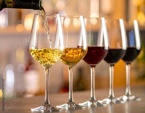 Wine being poured into glasses of varying color, on a bar-like setting with a soft bokeh
