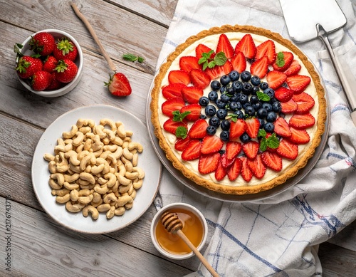 Top-down view of a fruit tart, ingredients, and utensils on a wooden surface