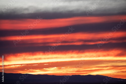 Fiery red and orange sunrise clouds over mountain range silhouette