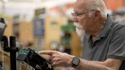 Photography An elderly man is at the self-checkout in a grocery store checking items and com