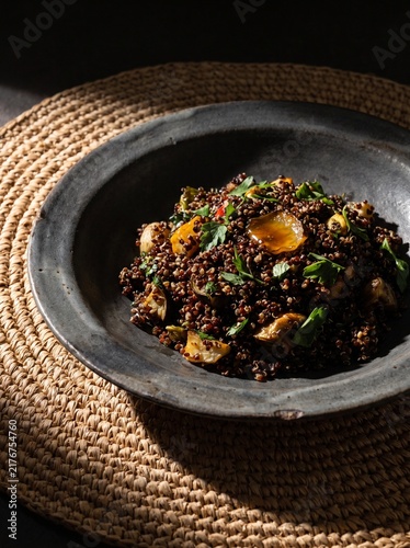 Healthy Red Quinoa Salad with Roasted Vegetables and Fresh Herbs in a Rustic Ceramic Bowl on a Woven Rattan Placemat, Dark Moody Food Photography for Restaurant Menu and Culinary Blog Content