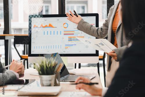 Businesswoman presenting data analysis graphs on computer screen to colleagues in office meeting