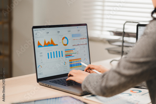 Businesswoman analyzing financial performance charts and dashboard data on laptop screen at office desk