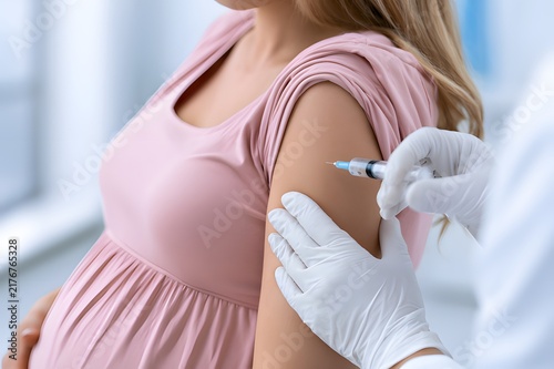 Doctor hands in white gloves giving vaccine injection to pregnant woman shoulder in clinic, prenatal healthcare support, maternal immunization campaign and seasonal flu protection concept