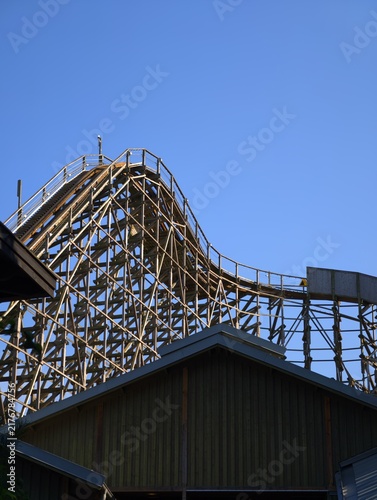 Photography Wooden roller coaster track climbing up a steep hill against a clear sky