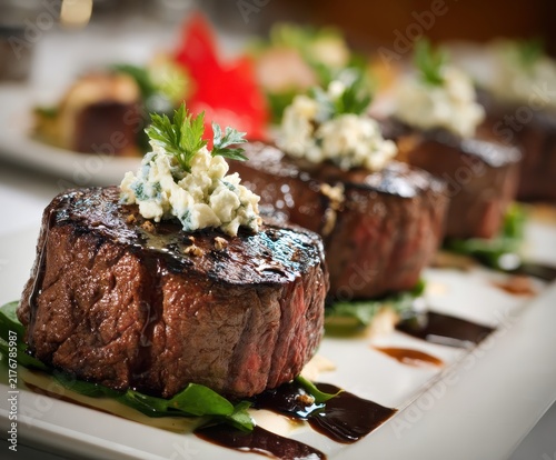 Gourmet Steak Presentation: Succulent, perfectly grilled steak medallions, each crowned with a dollop of creamy topping and fresh herbs, are elegantly arranged on a white platter.