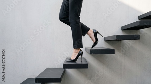 Ascending Ambition: A woman's legs in high heels ascend a modern staircase, symbolizing career progression and personal growth.